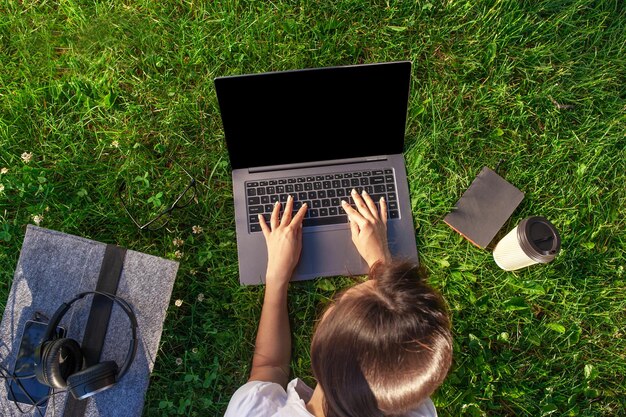 Bovenaanzicht. Vrouw die op laptop pc-computer werkt met een leeg zwart leeg scherm om ruimte in het park op groen graszonnegras buitenshuis te kopiëren.