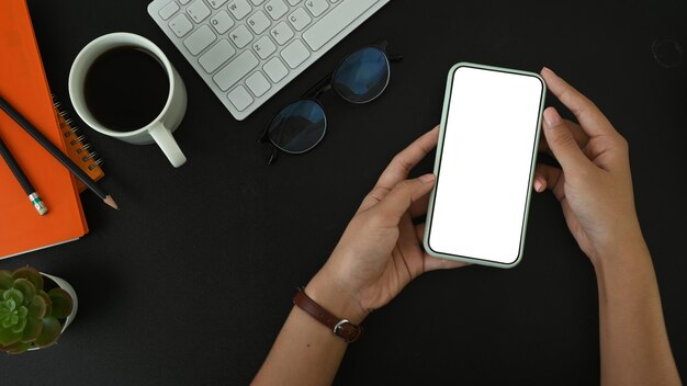 Bovenaanzicht vrouw handen met behulp van mobiele telefoon met wit scherm op zwart leer.