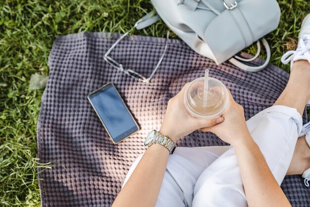 Bovenaanzicht vrouw met kopje met koel drankje zittend op deken op gras