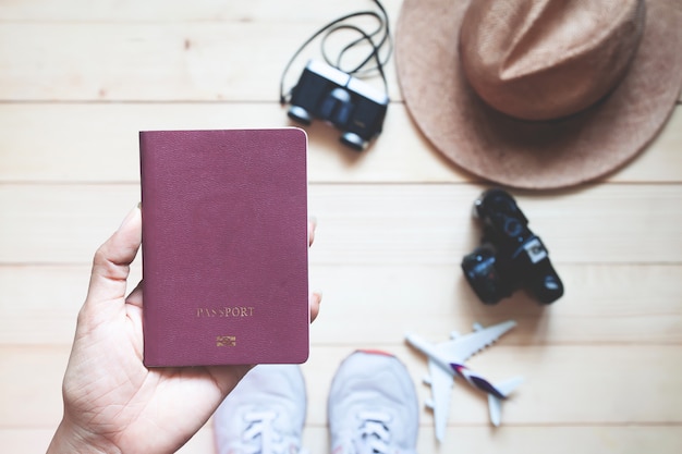 Bovenaanzicht vrouw met paspoort boek met camera&#39;s en hoed op houten vloer.
