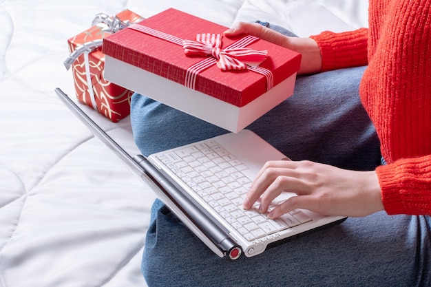 Bovenaanzicht vrouwelijke hand houdt een geschenkdoos en maakt aankopen op een laptop. vrouw koopt geschenken, bereidt zich voor op kerstmis, geschenkdoos in de hand. wintervakantie verkoop. kerst online winkelen.