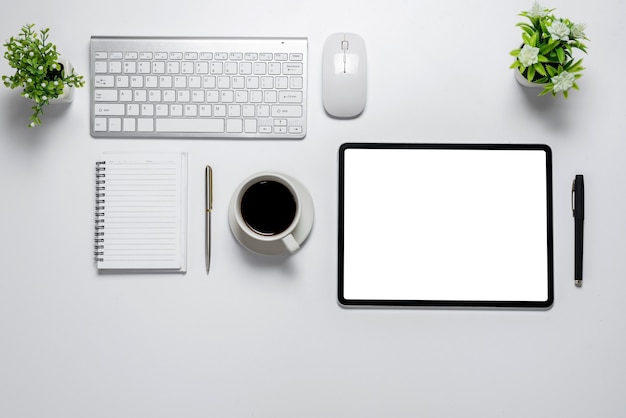 Bovenaanzicht wit bureau met tablet leeg wit scherm koffie toetsenbord muis notebook Op een witte tafel.