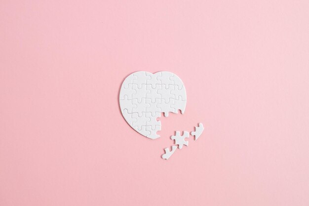 Bovenaanzicht witte hartpuzzel met een ontbrekend stuk op roze achtergrond
