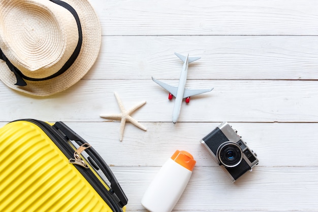 Foto bovenaanzicht zomerreizen en plan. gele koffer bagage met accessoires mode, oude camera, sunblock. reizen in de vakantie reizen vliegtuig op hout witte achtergrond in vakantiereizen.