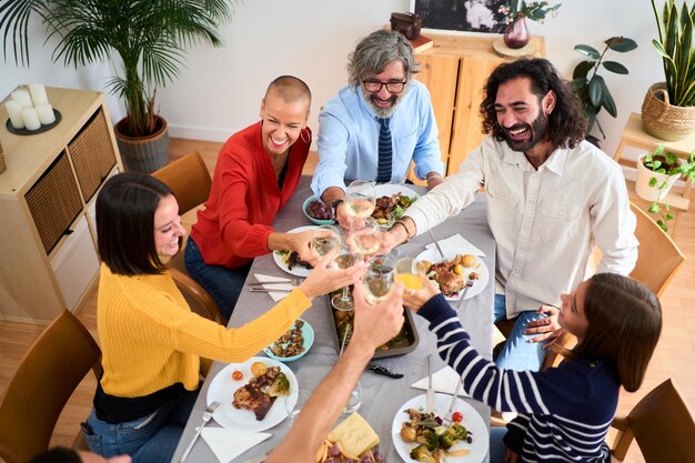 Foto bovenbeeld glimlachende blanke mensen bij een maaltijd, samen toasten met witte wijn en drinken aan tafel