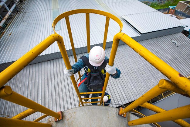 Foto bovenbeeld mannelijke werknemer klimt de ladder af inspectie roestvrij tank werk op hoogte veiligheidsharnas