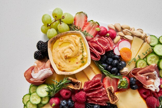 Bovenbeeld van een kaasbord met hummus, fruit en groenten op een witte achtergrond