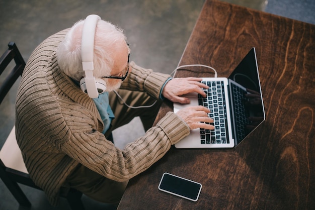 Bovenbeeld van een oudere man met een koptelefoon die een laptop gebruikt