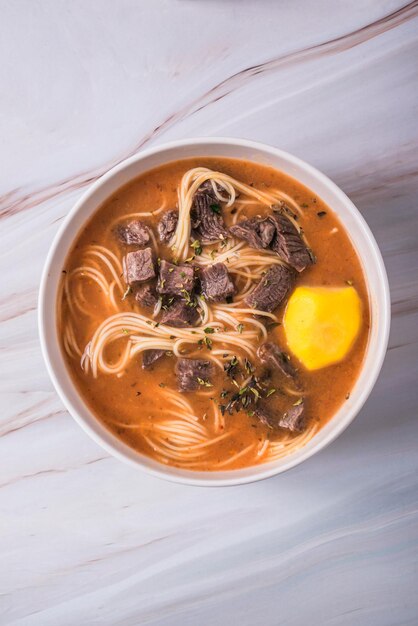 Foto bovenbeeld van een soep a la minute met dunne noedels tomaten gele aardappelmelk vlees en oregano