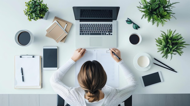 Bovenbeeld van een vrouw die aan haar bureau werkt. Ze is omringd door planten, een laptop, koffie en andere kantoorbenodigdheden.