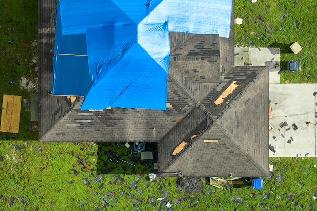 Bovenbeeld van het lekende dak van het huis bedekt met beschermende tarpplaten tegen regenwaterlekken tot de vervanging van asfaltgordel Schade aan het dak van het gebouw na de orkaan Ian in Florida