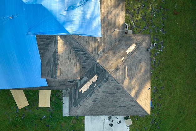 Bovenbeeld van het lekende dak van het huis bedekt met beschermende tarpplaten tegen regenwaterlekken tot de vervanging van asfaltgordel Schade aan het dak van het gebouw na de orkaan Ian in Florida
