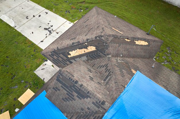 Bovenbeeld van het lekende dak van het huis bedekt met beschermende tarpplaten tegen regenwaterlekken tot de vervanging van asfaltgordel Schade aan het dak van het gebouw na de orkaan Ian in Florida