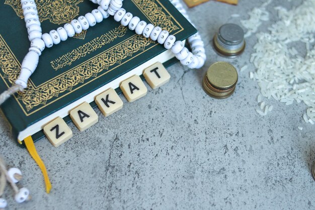 Foto bovenbeeld van islamitische gebedskralen op het heilige boek van de koran met gestapelde munten en houten kubussen met z