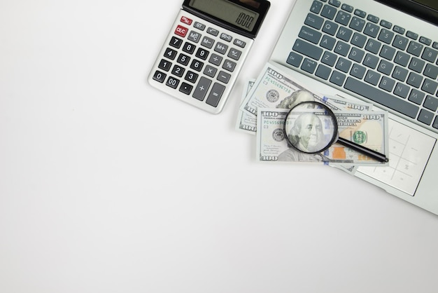 Bovenbeeld van laptop en rekenmachine met dollars op witte achtergrond