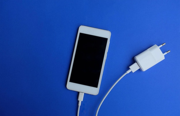 Bovenbeeld witte smartphone aansluiting met oplader adapter op blauwe achtergrond