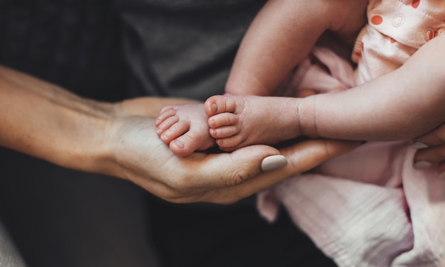 Bovenste meningsfoto van een blanke moeder die haar pasgeboren baby in handen houdt die haar benen met de palm aanraakt