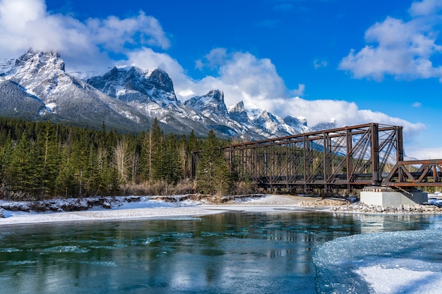 Bow River in winter sunny day. Snow capped Mount Rundle mountain range in background.