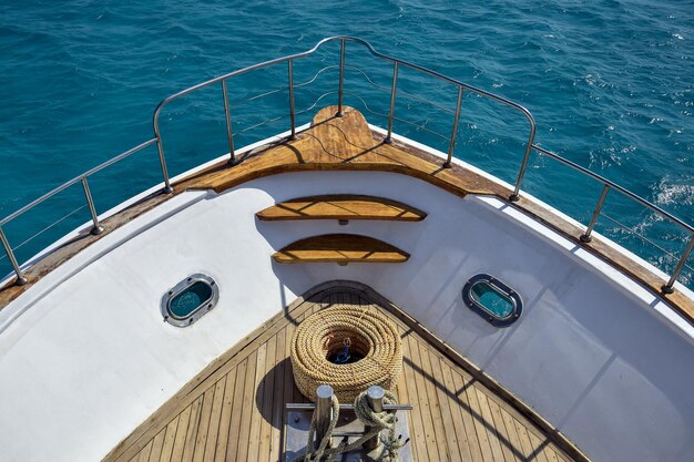 Bow of white yacht on background of blue sea bay with thick rope lies on wooden deck