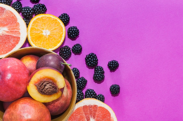 Ciotola di mela; pesca; arancia; uva frutta fette e more su sfondo viola