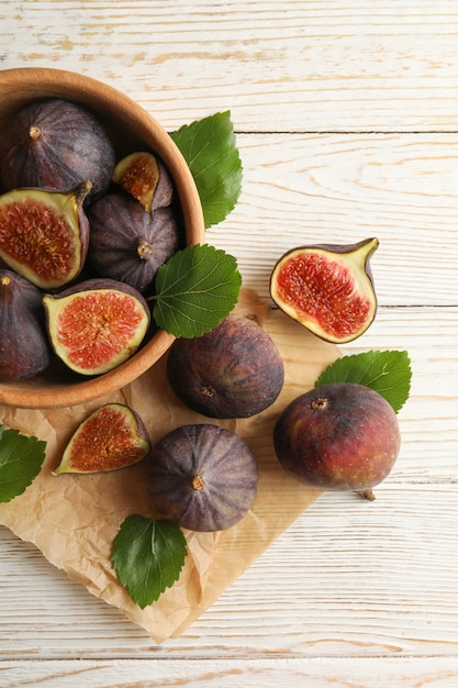 Bowl and baking paper with fig and leaves on white wood