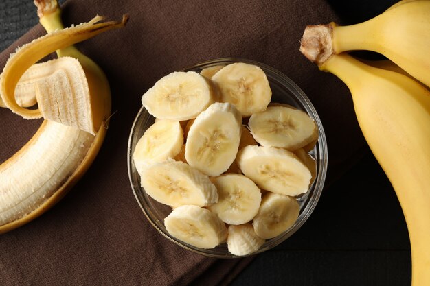 Foto ciotola di fette di banana, banana e asciugamano sul tavolo di legno