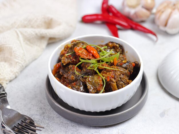 A bowl of beef stew with a red and green onion on top.