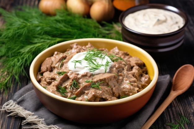 A bowl of beef stroganoff next to sour cream and herbs