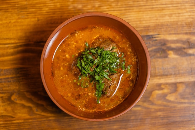 A bowl of beef vegetable soup garnished with dill and parsley.