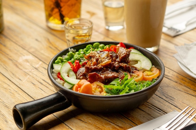 Photo a bowl of beef and vegetables sits on a table with a glass of iced tea.