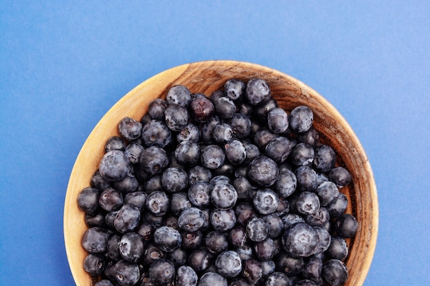 Bowl of blueberries in wooden bowl over blue isolated, Fresh berry.