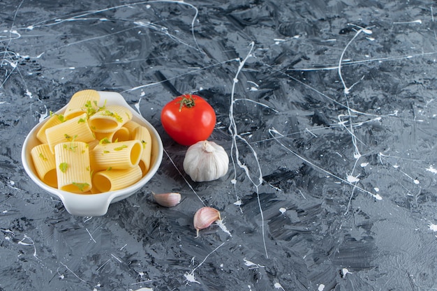 Bowl of boiled calamarata pasta with vegetables on marble background. 