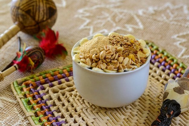 Bowl of Brazilian acai with granola peanuts and banana on a table with handicrafts from the Amazon region blurred in the background