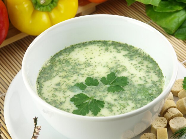 A bowl of broccoli soup with parsley leaves on the side