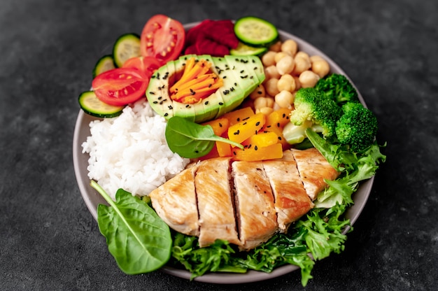 Foto bowl buddha. pollo, broccoli, ceci, zucca, avocado, carota, pomodoro, lattuga su un piatto con coltello e forchetta