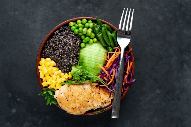 Bowl Buddha.Quinoa, chicken breast, arugula, avocado, red cabbage, carrot, green peas, corn, tomato, green beans in a white plate.