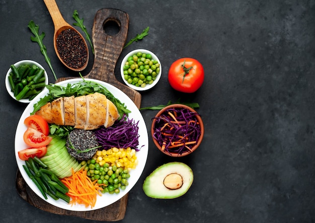 Photo bowl buddha.quinoa, chicken breast, arugula, avocado, red cabbage, carrot, green peas, corn, tomato, green beans in a white plate.