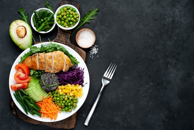 Bowl Buddha.Quinoa, chicken breast, arugula, avocado, red cabbage, carrot, green peas, corn, tomato, green beans in a white plate.