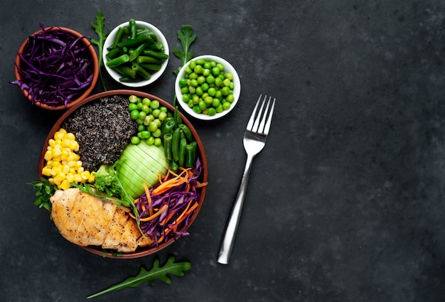 Bowl Buddha.Quinoa, chicken breast, arugula, avocado, red cabbage, carrot, green peas, corn, tomato, green beans in a white plate.