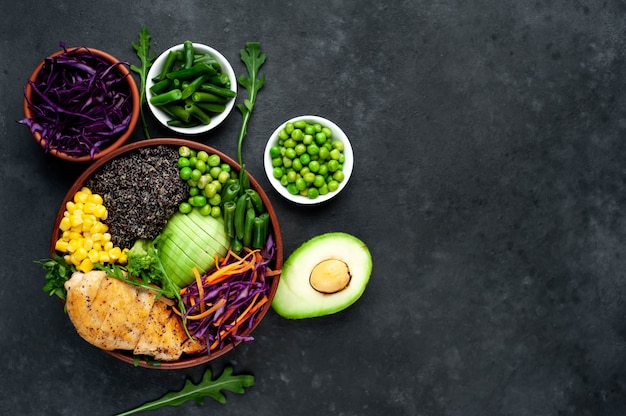 Bowl Buddha.Quinoa, chicken breast, arugula, avocado, red cabbage, carrot, green peas, corn, tomato, green beans in a white plate.