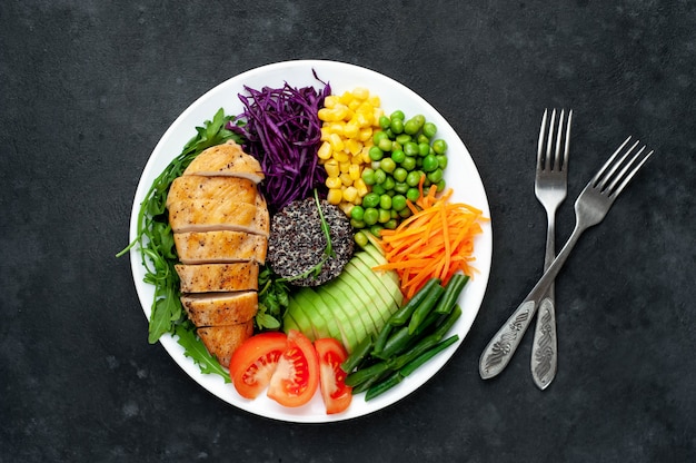 Bowl Buddha.Quinoa, chicken breast, arugula, avocado, red cabbage, carrot, green peas, corn, tomato, green beans in a white plate.