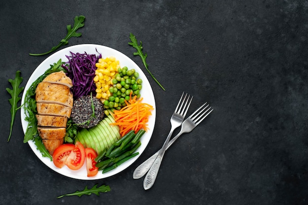 bowl buddha.quinoa, chicken breast, arugula, avocado, red cabbage, carrot, green peas, corn, tomato, green beans in a white plate.