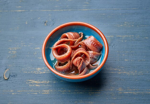 Bowl of canned anchovy fillets on blue wooden kitchen table