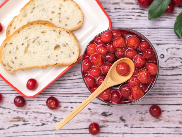 A bowl of cherry jam and bread of coarse flour on a wooden table