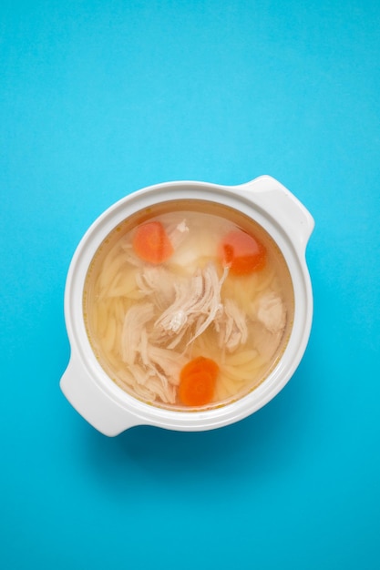 Bowl of chicken broth with chicken and carrot in blue