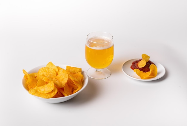 A bowl of chips and a glass of beer sit on a white table
