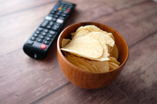 Ciotola di patatine e telecomando tv su sfondo di legno.