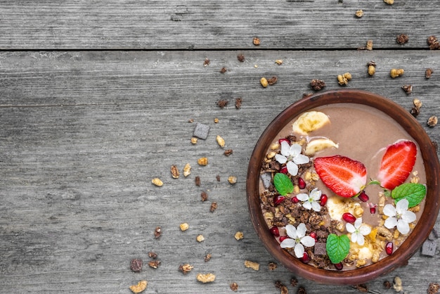 Ciotola di cioccolato e frullato di banana con muesli al cioccolato, fragole e semi di melograno decorati con fiori