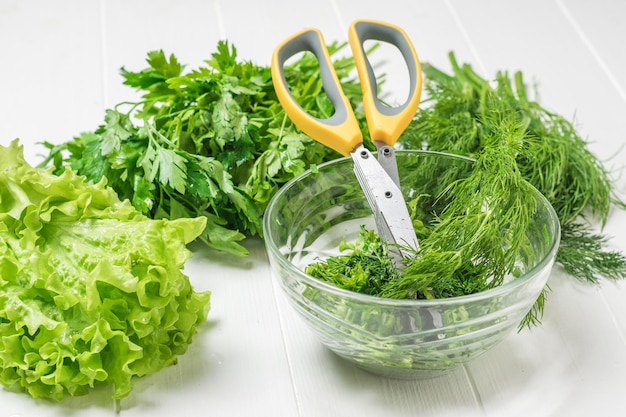 A bowl of chopped salad greens and scissors on a white table