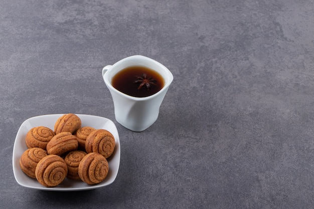 Bowl of cinnamon cakes and cup of tea on stone table.